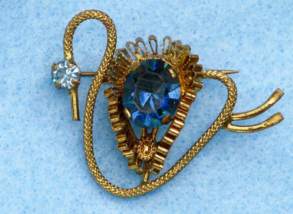 Photo of 1940s gold vintage brooch with big blue gemstone in the middle on blue background
