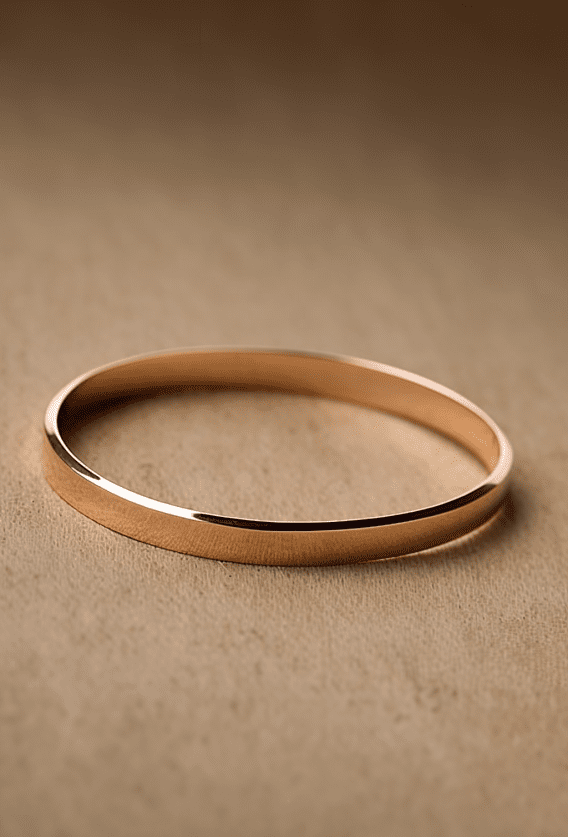 Image showcasing gold bangle bracelet on beige cloth surface.