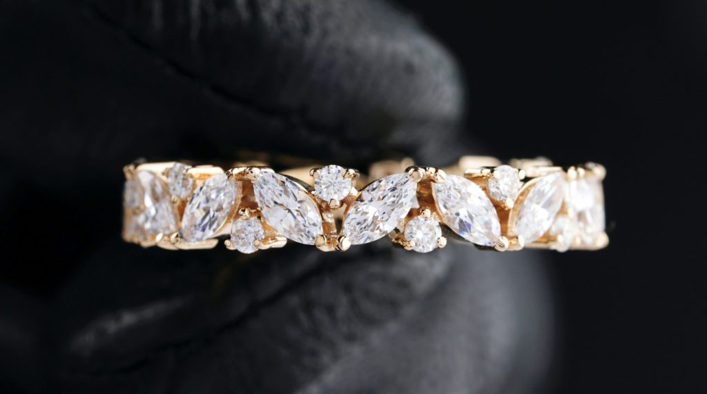 Imagine of gloved jewelers hand holding a diamond ring with gold metal band.