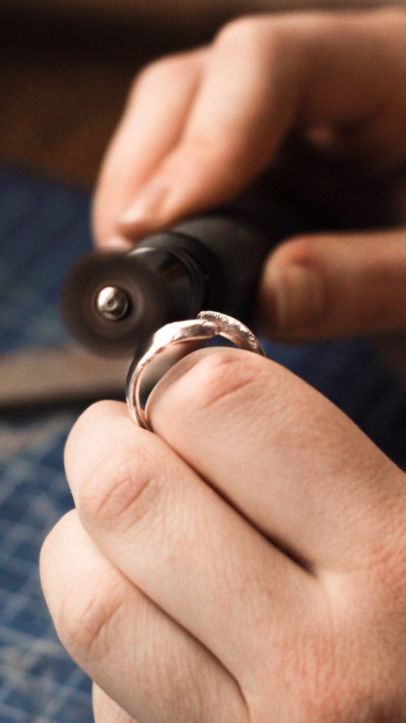Photo of jeweler's hands polishing silver ring with polishing tool.