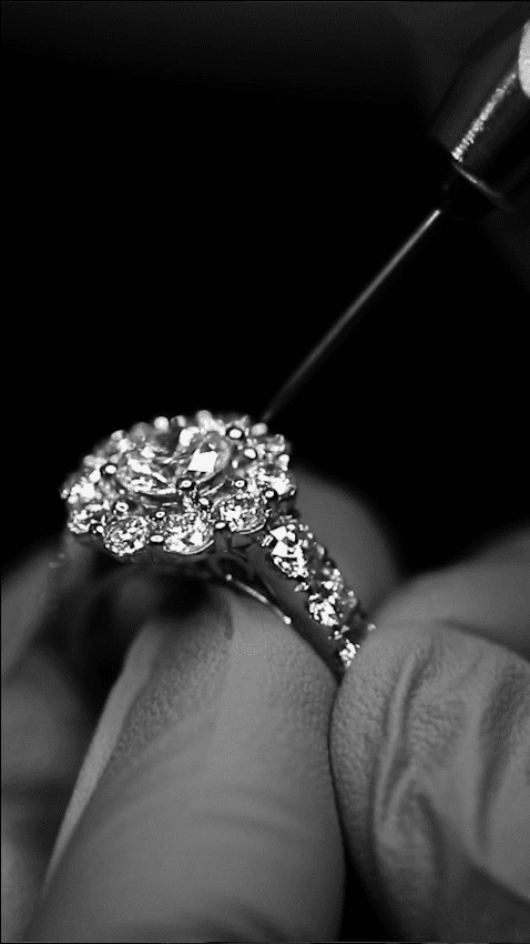 Black and white photo of diamond ring being held by gloved hand and ring repair tool on the other hand
