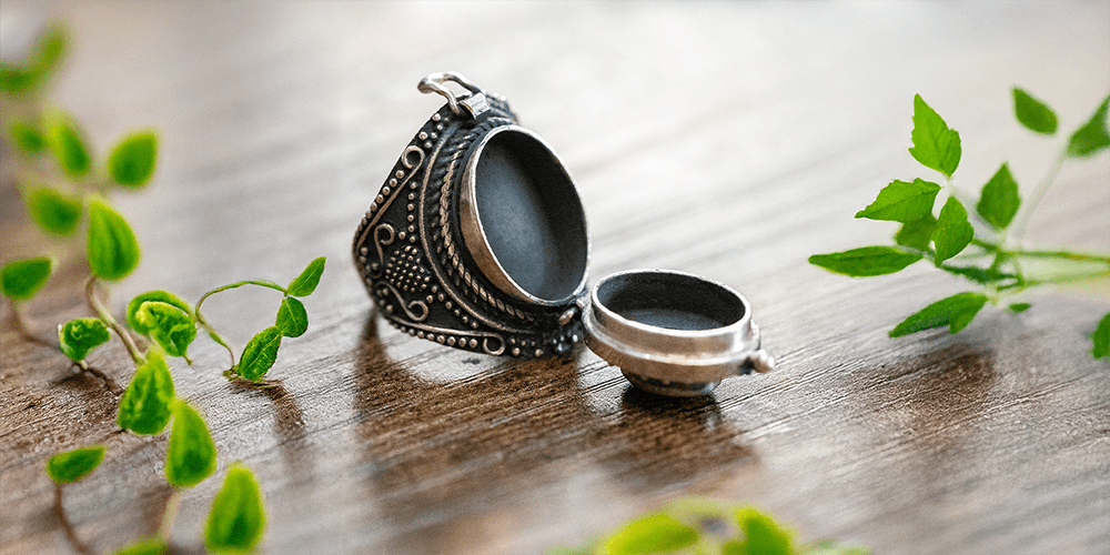 Silver Poison Ring with Red Gemstone Open and Displayed on Wooden Table with Greenery