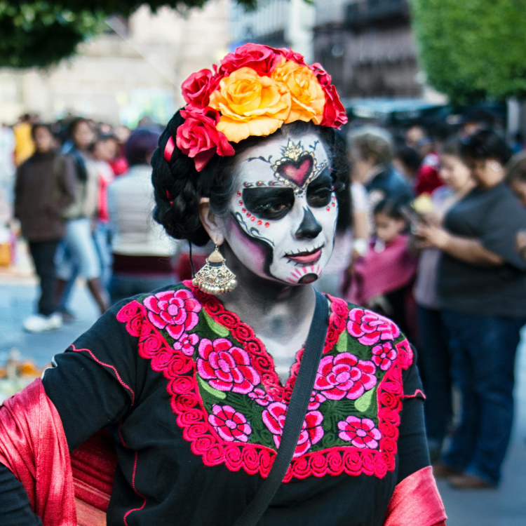 Image of woman wearing day of the dead skull makeup, flower crown, and large earrings